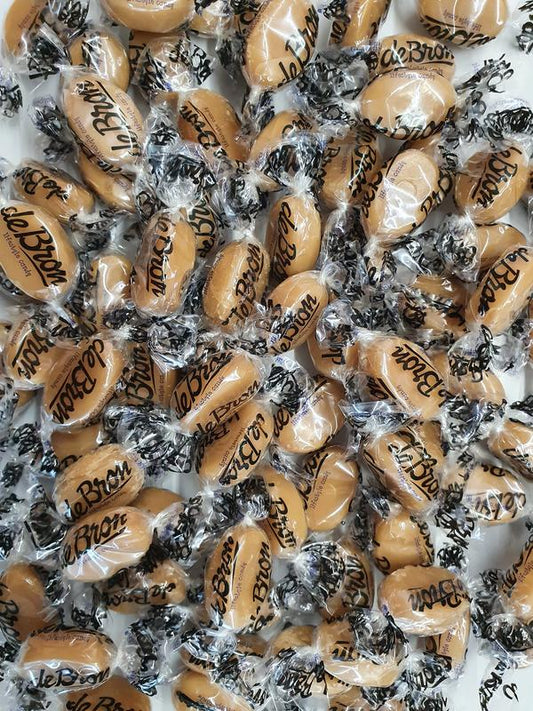 De Bron boterbabbelaars suikervrij snoepgoed in 2500 gram verpakking, showing golden caramel candies on a clear dish.