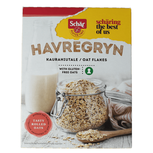 Schar glutenvrije havervlokken ontbijtgranen in een witte kom, met een lepel en een glas melk op de achtergrond.